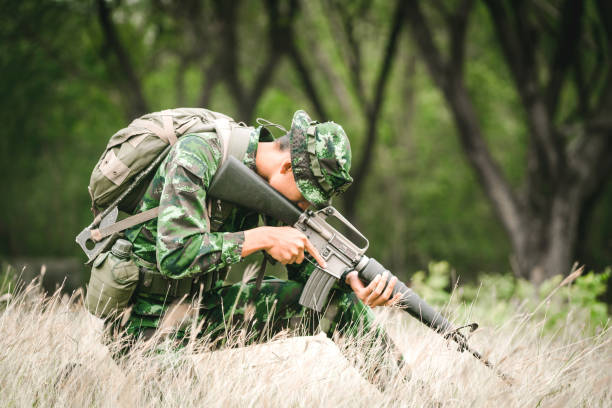 żołnierz siedzący na ziemi i kamuflaż w trawie. żołnierz trzymający broń i waring armor uniform. wojsko jest odpowiedzialne za utrzymanie terytorium. - cloaking zdjęcia i obrazy z banku zdjęć