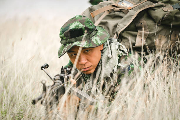 żołnierz leżący na ziemi i kamuflaż w trawie. żołnierz trzymający broń i waring armor uniform. wojsko jest odpowiedzialne za utrzymanie terytorium. - cloaking zdjęcia i obrazy z banku zdjęć