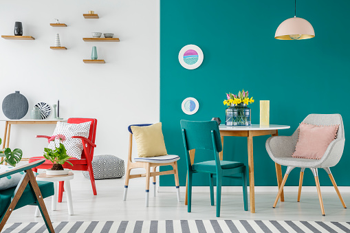 Chairs at wooden table against green wall in colorful apartment interior with flowers