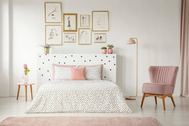 istock Framed posters gallery above a cozy double bed in a feminine room interior with a comfy, retro armchair 995746218