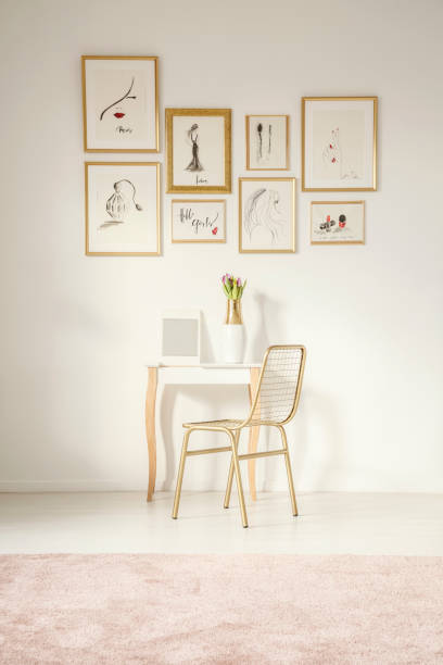 golden chair by an elegant vanity with a mirror by a white wall with drawings gallery in a feminine bedroom interior with a pink rug - fotografia imagem imagens e fotografias de stock