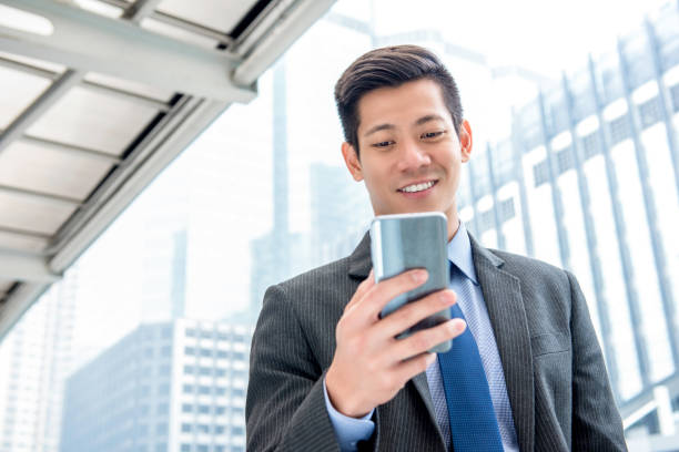 istock Young handsome Asian businessman  using mobile phone outdoors 995746490