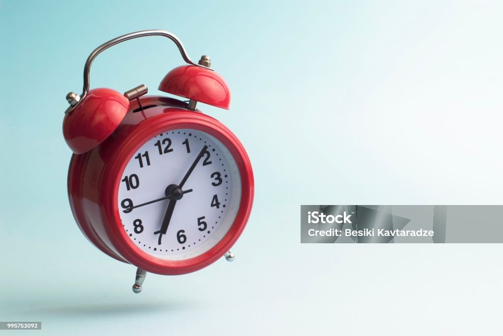 Red alarm clock jumping Red alarm clock on blue Alarm Clock Stock Photo