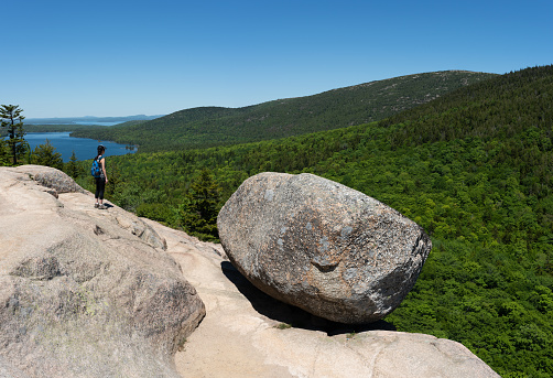 A female hiker reaches the top of Bubble Rock Trail in Acadia National Park, Maine.
