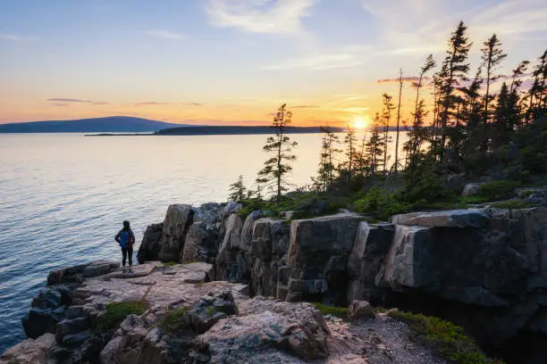 A female hiker watching the setting sun at Ravens Nest on the Schoodic Peninsula in Acadia National Park, Maine.