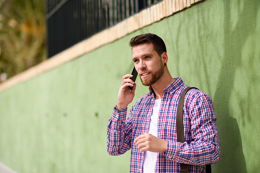 Young man talking with his smart phone in urban background. Guy wearing casual clothes. Lifestyle concept.