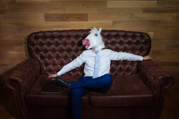 istock Funny unicorn in suit sits on sofa like a boss 995771312