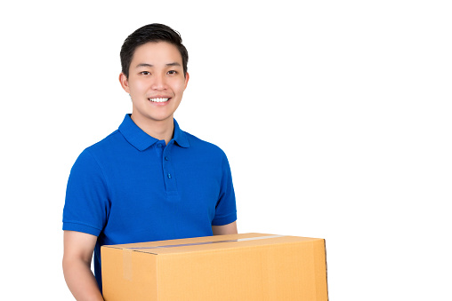 Handsome friendly smiling Asian delivery man  in blue polo shirt carrying parcel box, studio shot isolated on white background