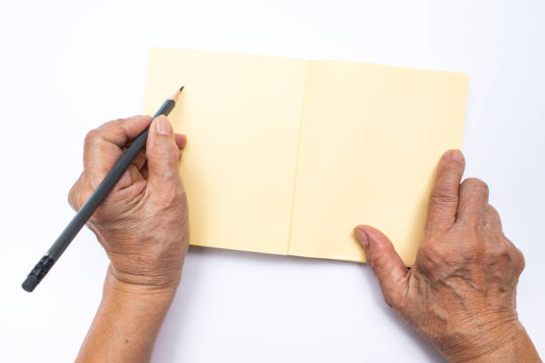 グレーと年配の女性の左手鉛筆ホワイト バック グラウンド、文房具の概念に分離されたノートに書く - copy space left ストックフォトと画像