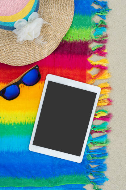 istock Hat and sunglasses with tablet on colorful cloth on white sand beach, Top view 995883816