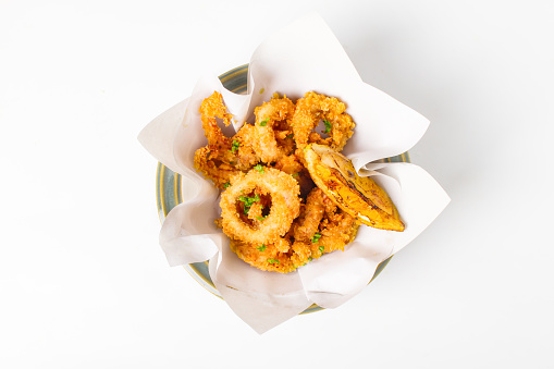 Fried crispy squid rings breaded ( caramari ) with lemon top view in a paper on white backgruond