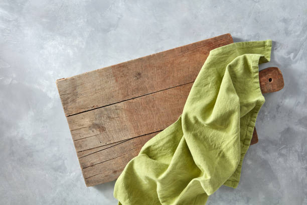 A wooden board with a green kitchen napkin on a gray concrete background with a copy space. Top view