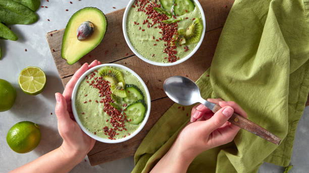 istock Dietary smoothies from green vegetables with flax. A woman's hand holds a plate with a smoothie and a spoon on the background of a gray kitchen table. Top view 995910042