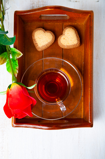 Heart-shaped biscuits, rose and tea on a wooden tray for St. Valentine's Day. Romantic breakfast.