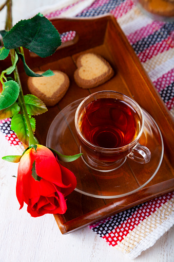 Heart-shaped biscuits, rose and tea on a wooden tray for St. Valentine's Day. Romantic breakfast.