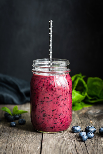Fresh acai blueberry smoothie in bottle on wooden table over black background. Closeup view, selective focus. Concept of healthy lifestyle, healthy eating, dieting, raw diet and vegan food