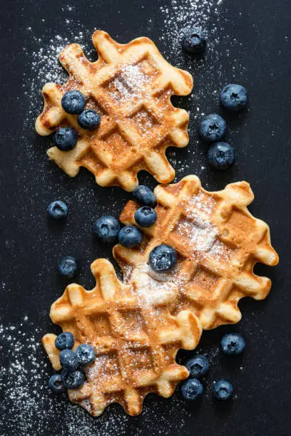 Photo of Waffles with blueberries and sugar on slate, top view