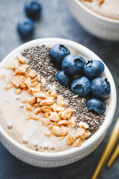 istock Smoothie bowl with banana, chia seeds, fresh blueberry and nuts over grey table. 995937644