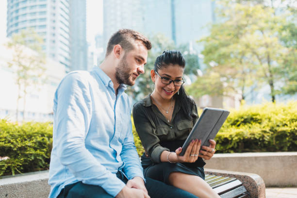 istock Two businesspeople using a digital tablet and sitting on a bench in the park 995955770