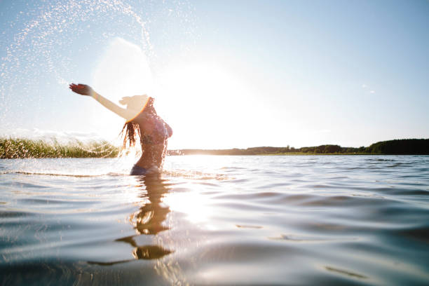 jovem mulher no lago, salpicos de água, braços levantados, acesas volta - life back lit people happiness - fotografias e filmes do acervo