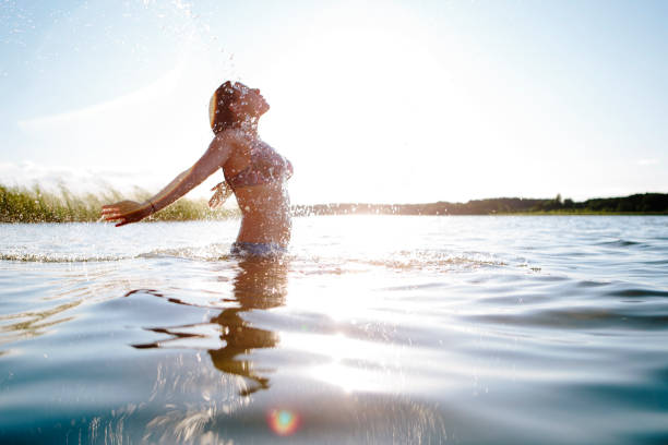 jovem mulher no lago, salpicos de água, braços levantados, acesas volta - life back lit people happiness - fotografias e filmes do acervo