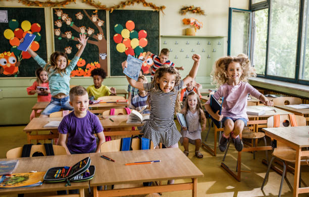istock Cheerful school children having fun while jumping among desks in the classroom. 995987214