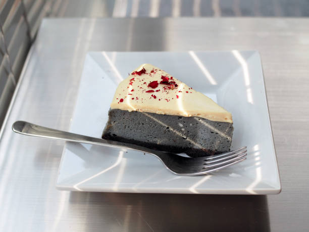 A white plate of homemade charcoal cheesecake topped with rose petal on table background.