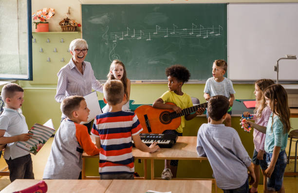Music class at elementary school! Happy senior teacher singing with large group of elementary students whole are playing musical instruments on a lass. music theory stock pictures, royalty-free photos & images