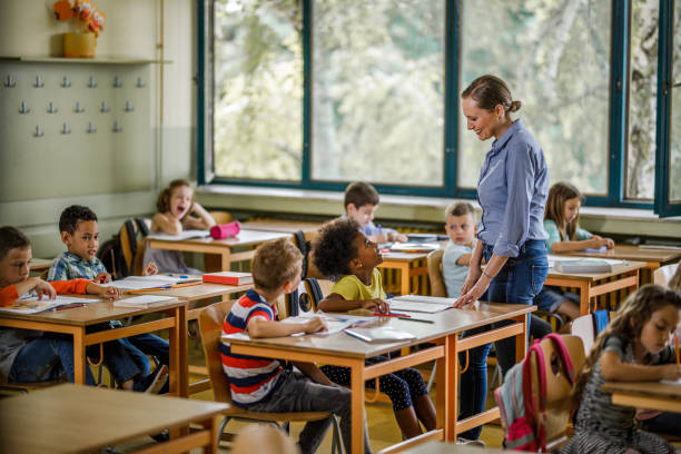 istock Happy elementary teacher talking to kids in the classroom. 996002326