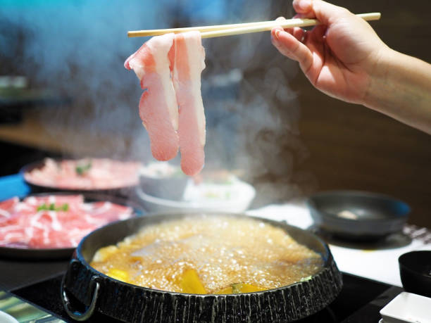 istock Picking thin sliced pork meat or bacon with chopsticks over hot pot, shabu or sukiyaki or Japanese hot pot. 996005708