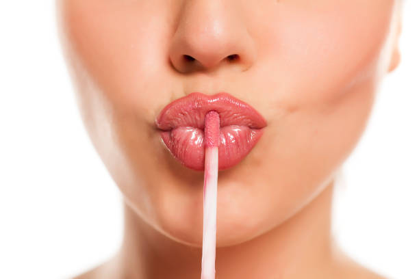 young beautiful woman apply a lip gloss on her lips on white background stock photo