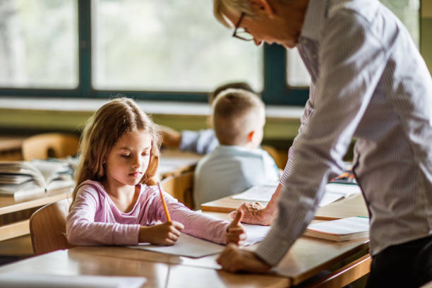istock Elementary student writing with assistance of her female teacher. 996015374