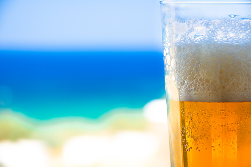 Glass of cold beer on blurred aegean sea background, Greece.