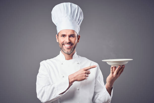 Smiling chef holding plate and pointing on it. Isolated