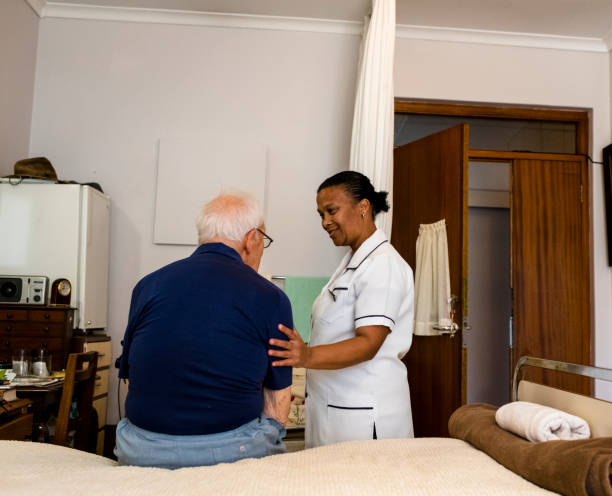 istock Senior man sitting on a bed with nurse comforting him 996053540