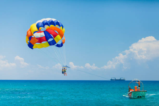 Couple of tourists flying on a colorful parachute Parasailing water amusement - flying on a parachute behind a boat on a summer holiday by the sea in the resort parasailing stock pictures, royalty-free photos & images