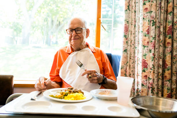 老人ホームで笑みを浮かべて年配の男性が食べる昼食の肖像画 - senior adult nursing home eating home interior ストックフォトと画像