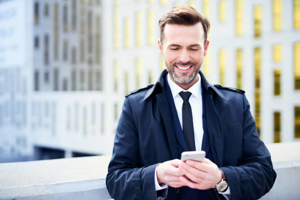 istock Smiling businessman using phnoe standing outdoors 996061994