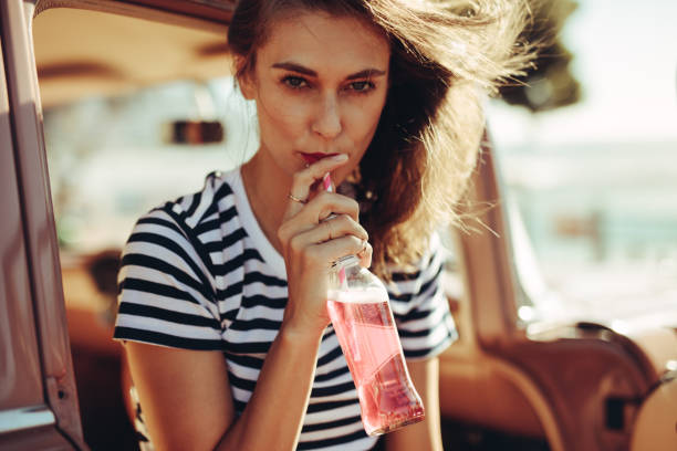 Woman drinking beverage on road trip Young caucasian woman drinking beverage with straw from a glass bottle. Female drinking refreshing soft drink in the car. soda bottle stock pictures, royalty-free photos & images