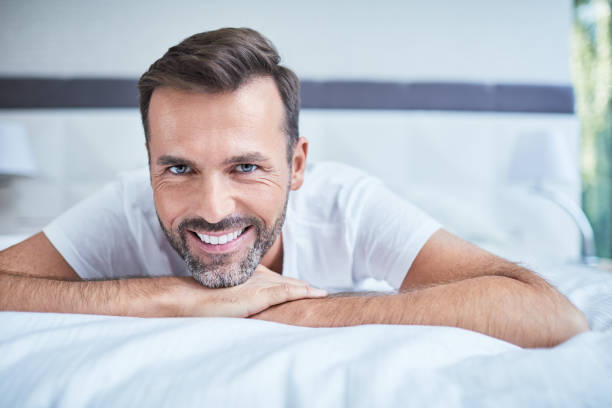 istock Portrait of smiling man lying on bed and looking at camera 996083596