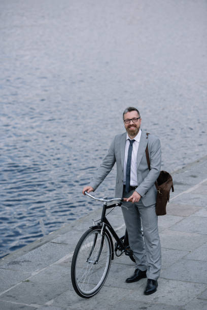 istock handsome businessman with leather bag standing on quay with bicycle 996083712