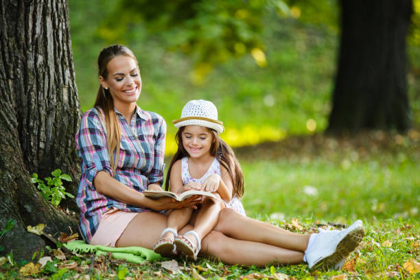 istock Mother and daughter sitting on grass reading a book 996084228
