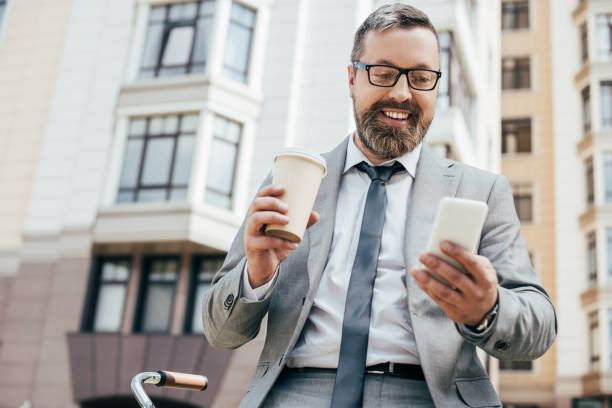 istock bearded businessman using smartphone and holding paper cup of coffee 996088582