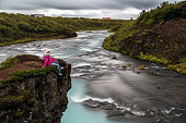 Young woman relaxing on a cliff and enjoying the view at Bruarfoss waterfall, Iceland.