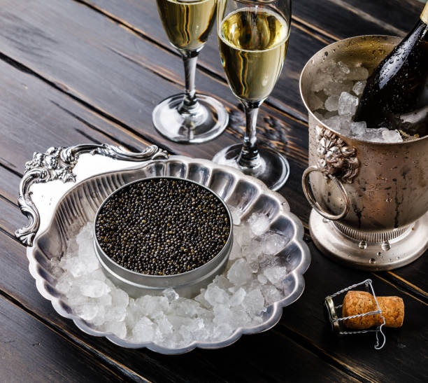 Black caviar in can on ice in silver bowl and champagne