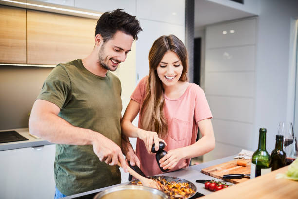 urocza radosna para gotując razem i dodająca pikanterii do posiłku, śmiejąc się i spędzając razem czas w kuchni - cooking men caucasian togetherness zdjęcia i obrazy z banku zdjęć