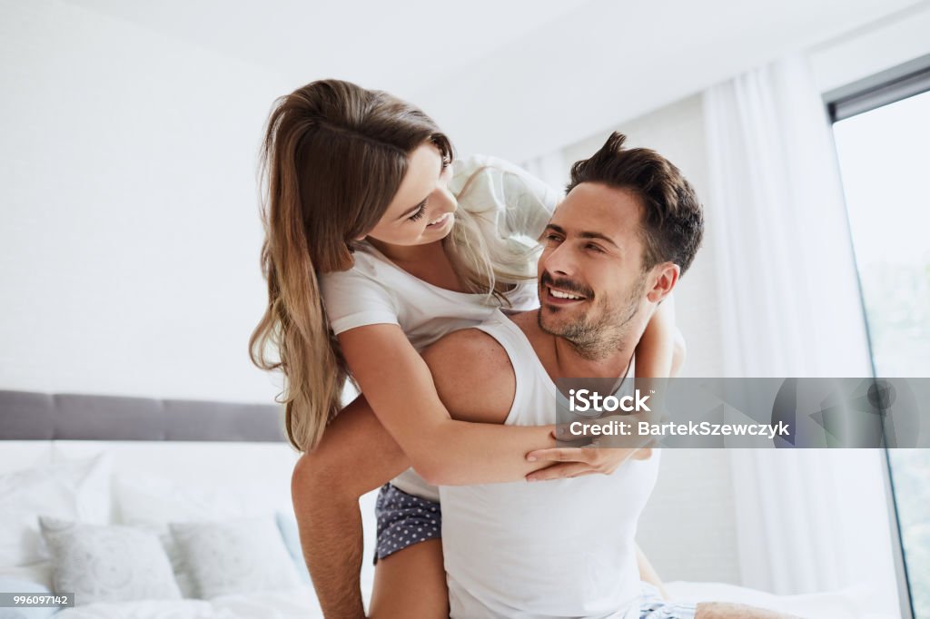 Young loving couple embracing and having fun sitting on bed in the morning Couple - Relationship Stock Photo