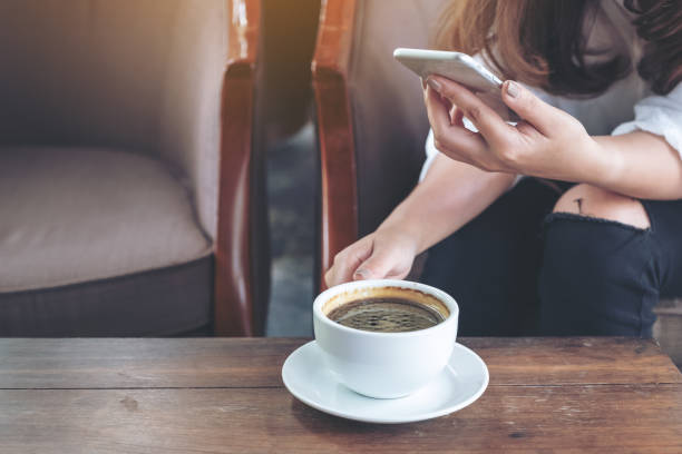 istock Closeup image of a woman holding , using and touching a smart phone while drinking coffee in cafe 996101056