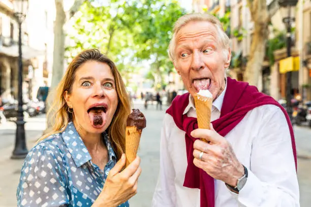 Senior couple eating ice cream and having fun in Barcelona. Adult woman and man making funny faces and grimacing while enjoying a fresh ice cream on a hot summer day in Spain. Summer and food concepts
