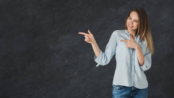 istock Happy woman pointing away on gray background 996172822